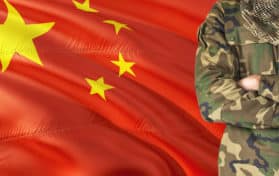Crossed arms Chinese soldier with national waving flag on background