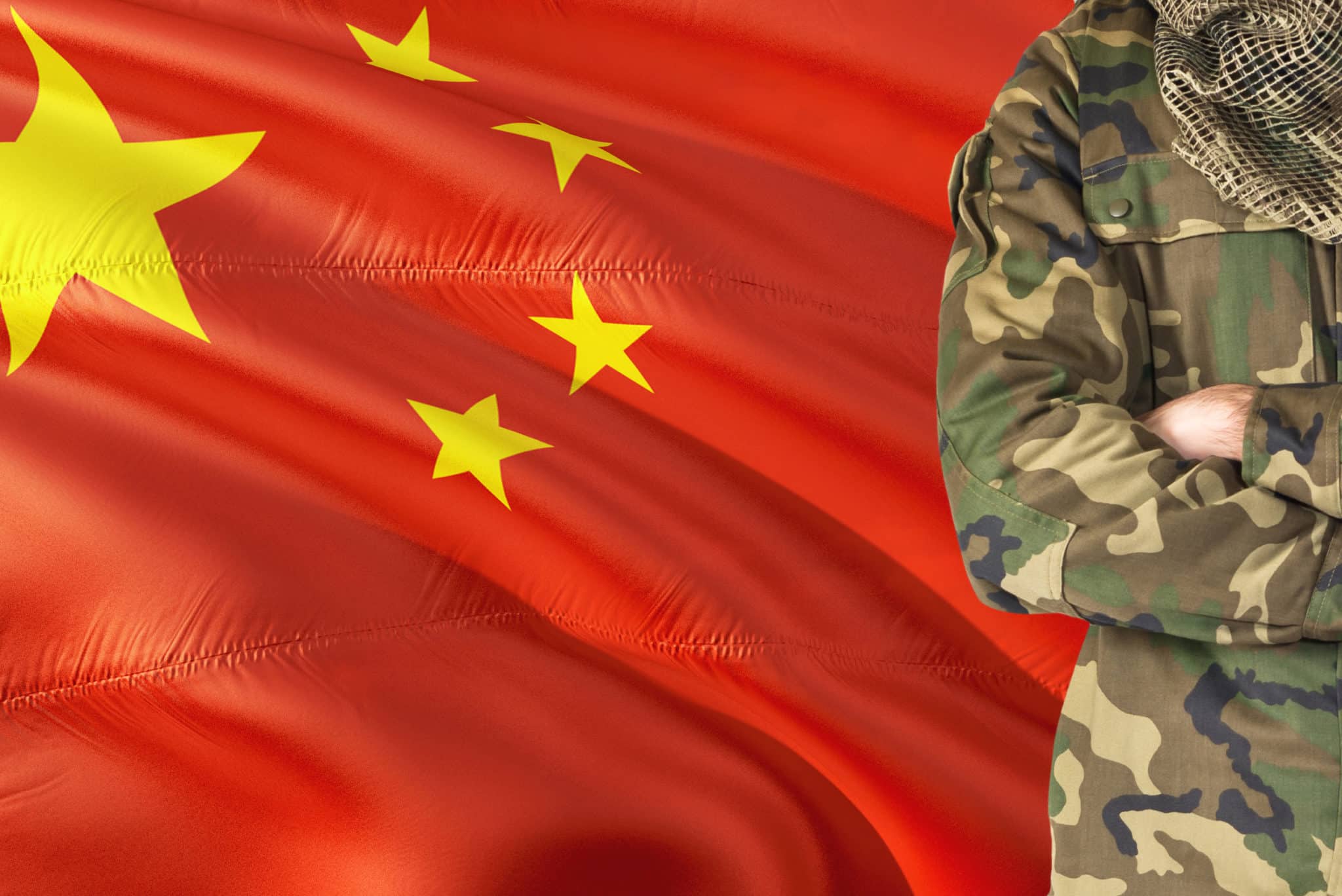Crossed arms Chinese soldier with national waving flag on background